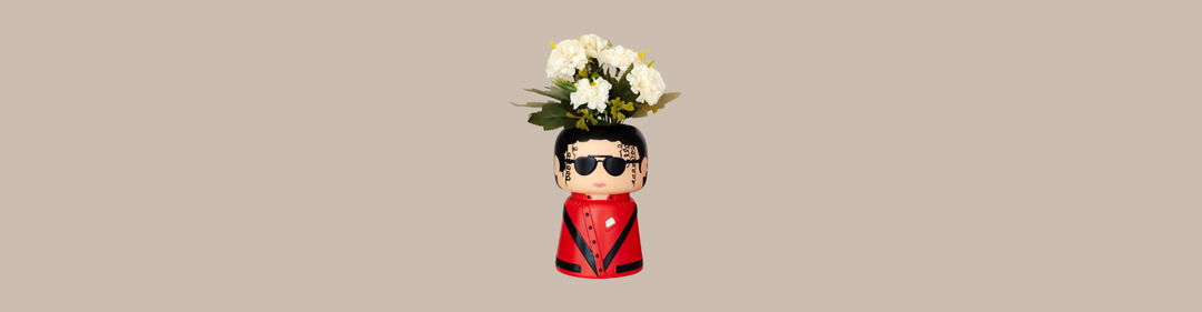 Vaso decorativo a forma di Michael Jaxkson in giacca rossa e occhiali da sole neri, con fiori bianchi posti sulla testa, su sfondo beige.