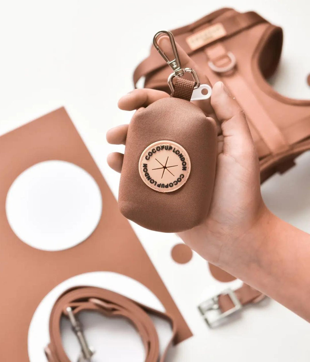 Porta Sacchetti brownie tenuto in mano, con collare e guinzaglio abbinati sullo sfondo.