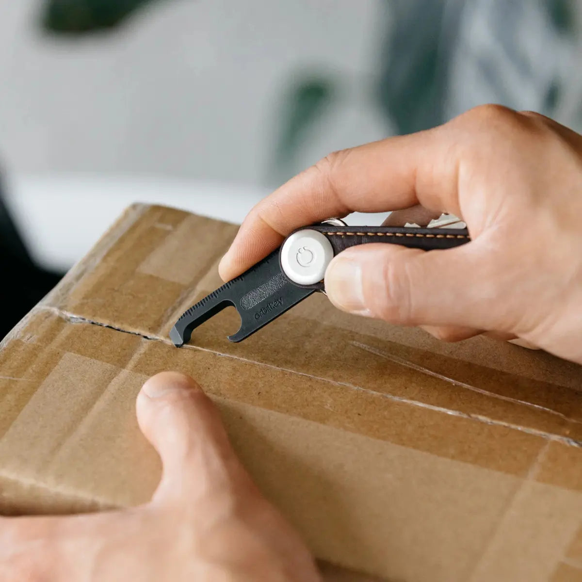 Accessorio multiuso orbitkey inserito nel portachiavi compatto utilizzato per aprire un pacco di cartone con del nastro adesivo