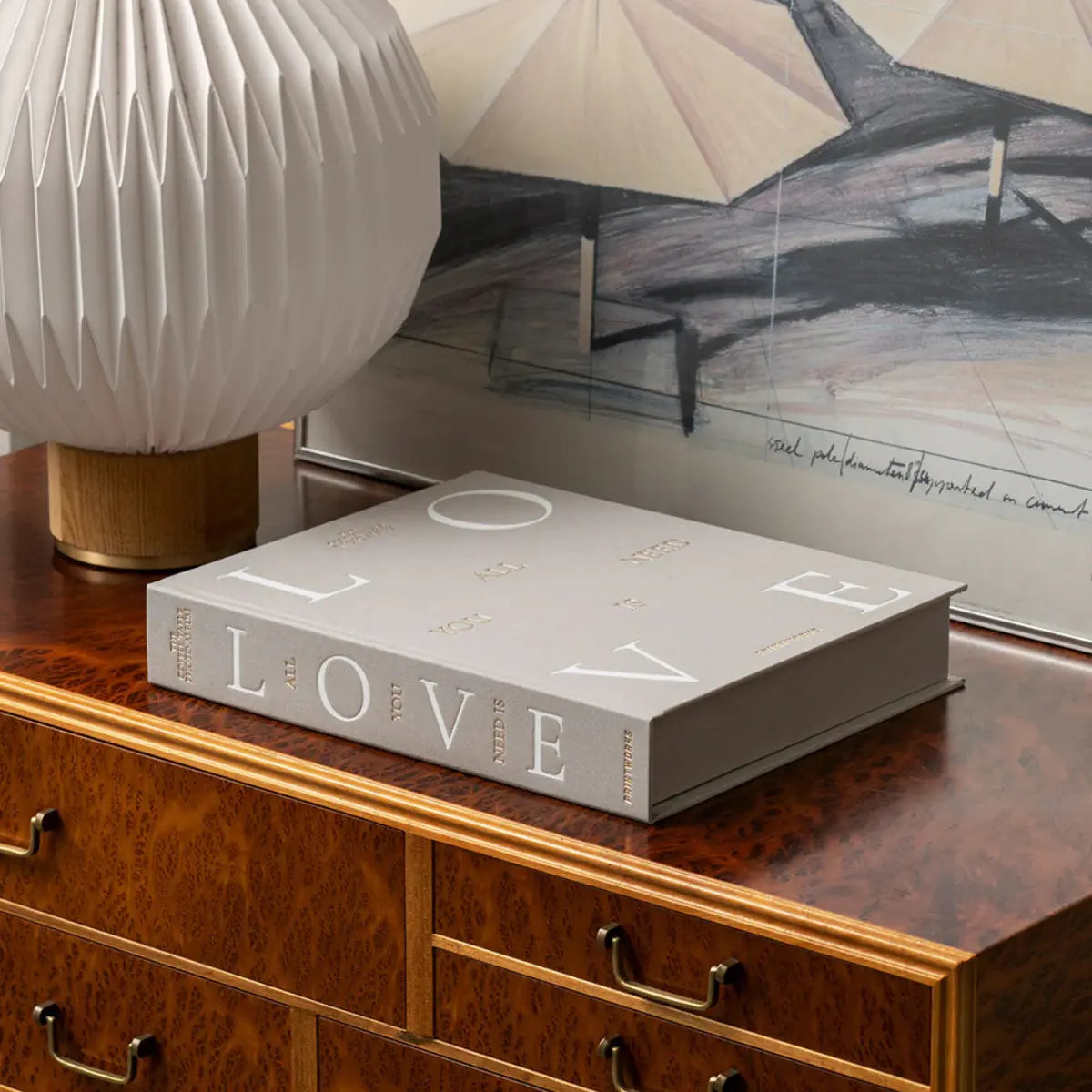 Album fotografico in tessuto grigio con scritte All You Need Is Love in oro e bianco appoggiato su un mobile di legno