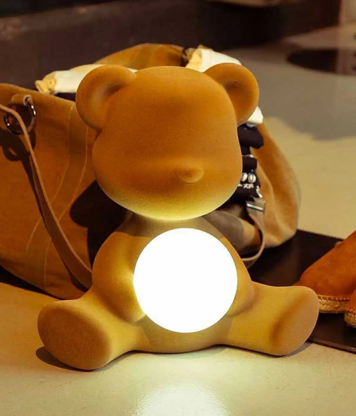 Lampada a forma di orsetto senape con sfera che s'illumina al centro di Qeeboo posizionata su tavolo