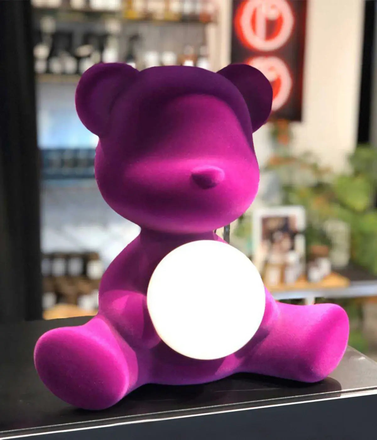 Un orsetto viola in velluto con sfera di luce accesa al centro. Sfondo finestra con panorama