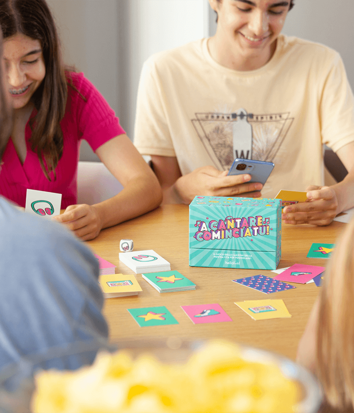 Tavolo con carte e scatola A Cantare Comincia Tu, ragazzi che giocano insieme.