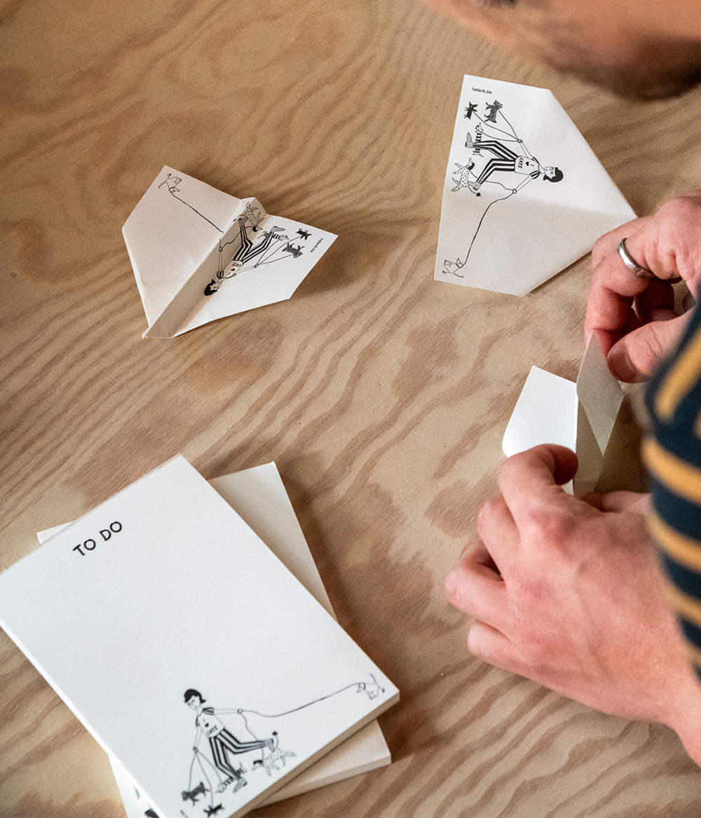 Mani che fanno gli aeroplani con i fogli bianchi con disegno del Blocknote. Sfondo legno.