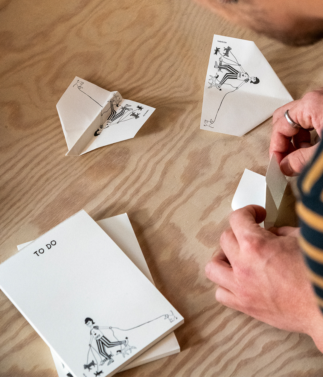 Mani che fanno gli aeroplani con i fogli bianchi con disegno del Blocknote. Sfondo legno.