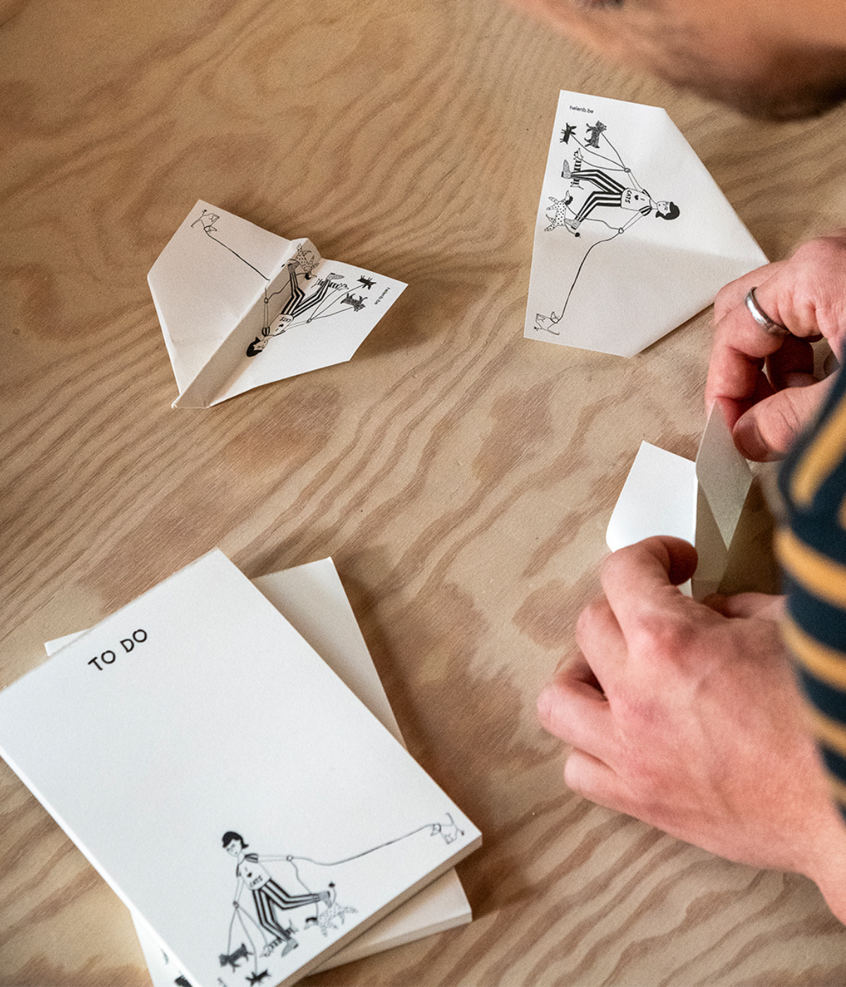 Mani che fanno gli aeroplani con i fogli bianchi con disegno del Blocknote. Sfondo legno.