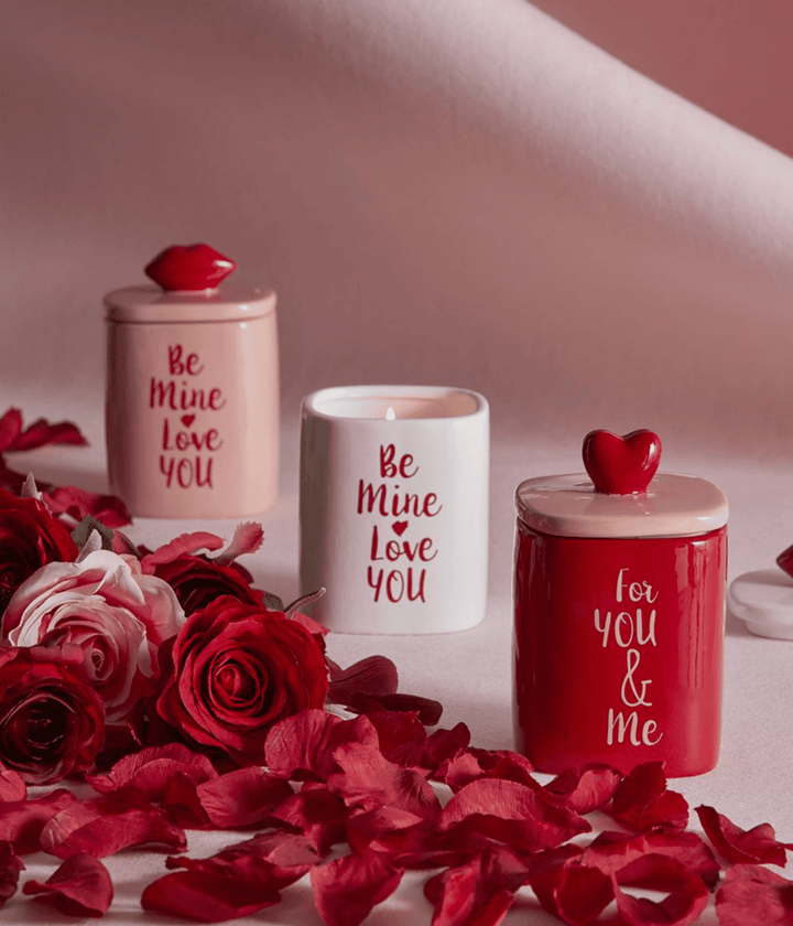 Candela rosa e bianca con scritta rossa Be Mine Love You e candela rossa For You and Me, sfondo rosa con rose rosse.
