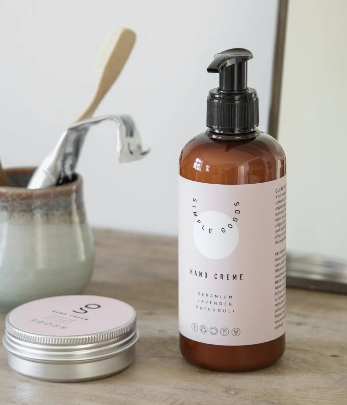 Un despencer marrone con etichetta rosa. Scritte nere Simple Goods e Hand Cream. Ambiente bagno