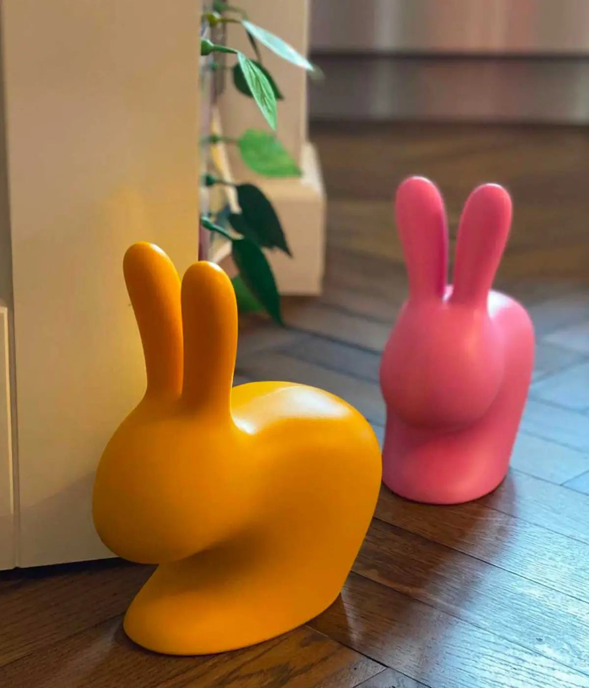 Due conigli fermaporta giallo e rosa. Sfondo pavimento marrone e pianta