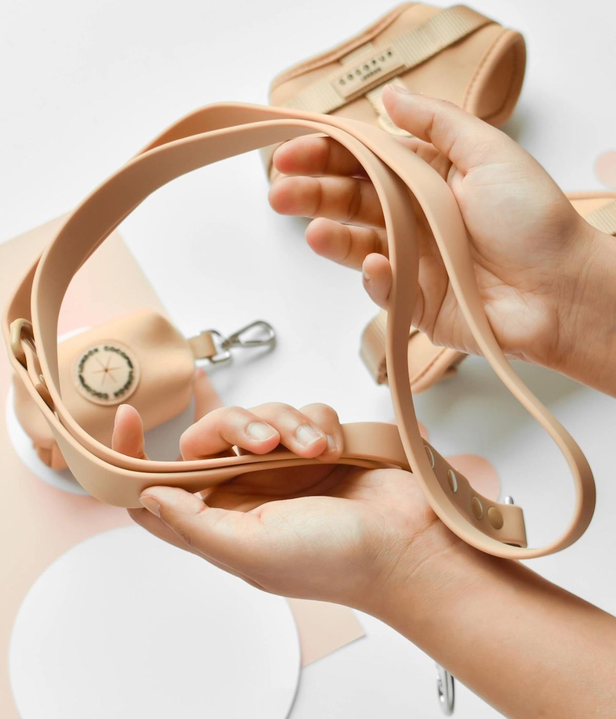 Primo piano guinzaglio per cani color biscotto. Sullo sfondo pettorina e porta sacchetti