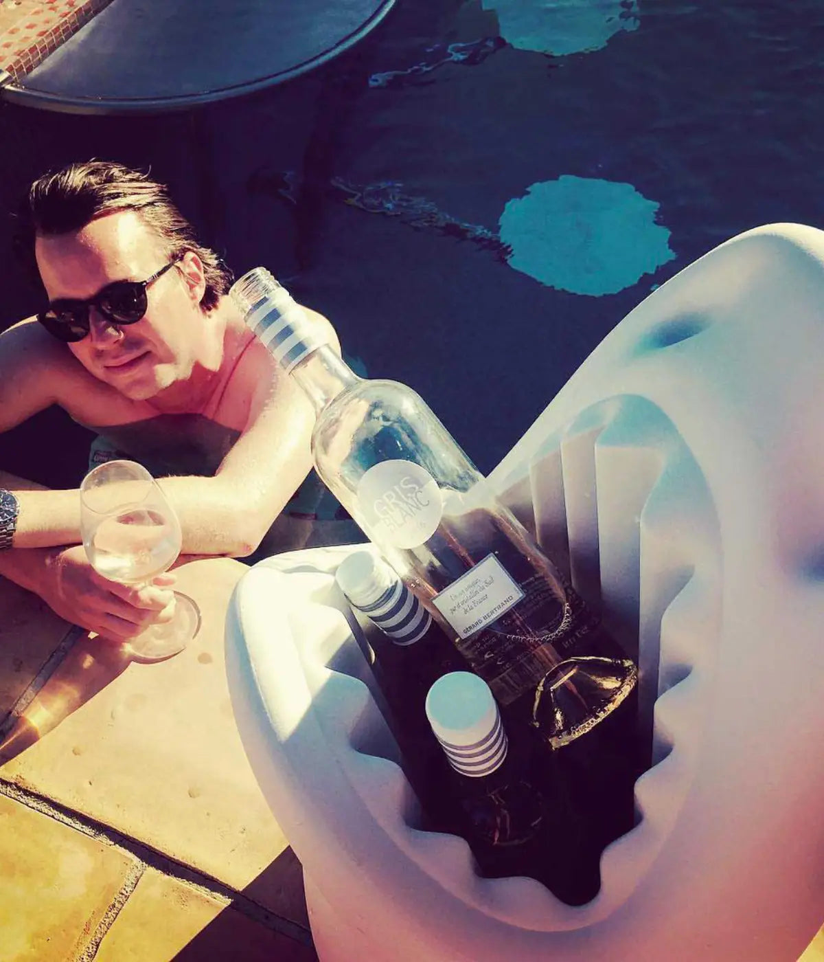 Squalo grigio chiaro in plastica a bordo piscina che contiene delle bottiglie. Sfondo bianco