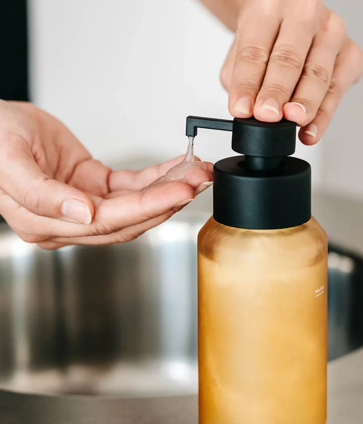 Mano che prende il sapone dal dispenser giallo ocn beccuccio nero. Sfondo immagine bagno