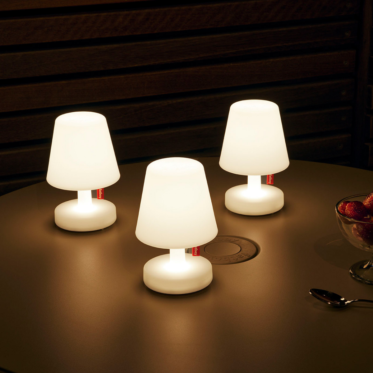 Tre lampade bianche accese con etichetta Fatboy rossa, appoggiate su tavolo con fragole e cucchiaio