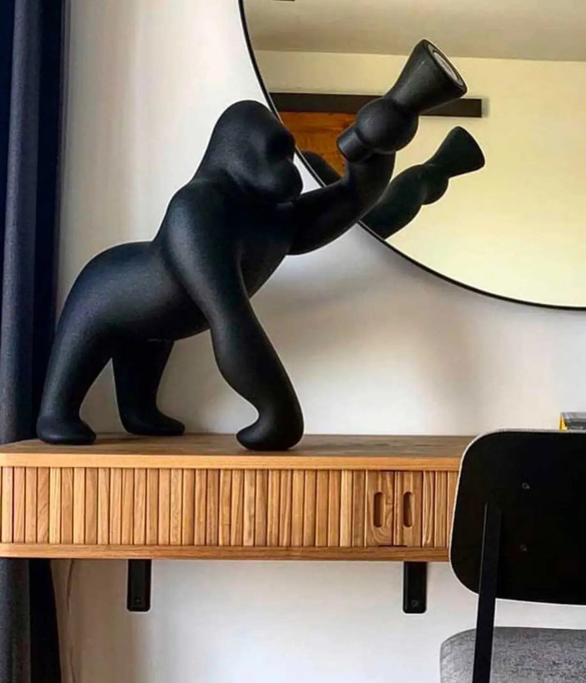 Lampada a forma di Kong appoggiata su scrivania. Specchio e sedia. Sfondo muro bianco