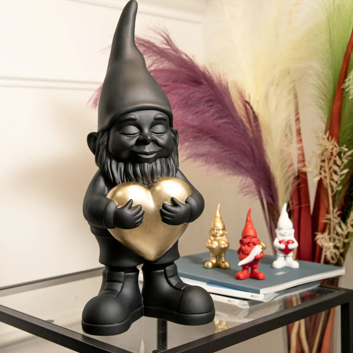 Nano nero con cuore oro, appoggiato su libreria in vetro. Sullo sfondo nano lover bianco, oro 12 cm.