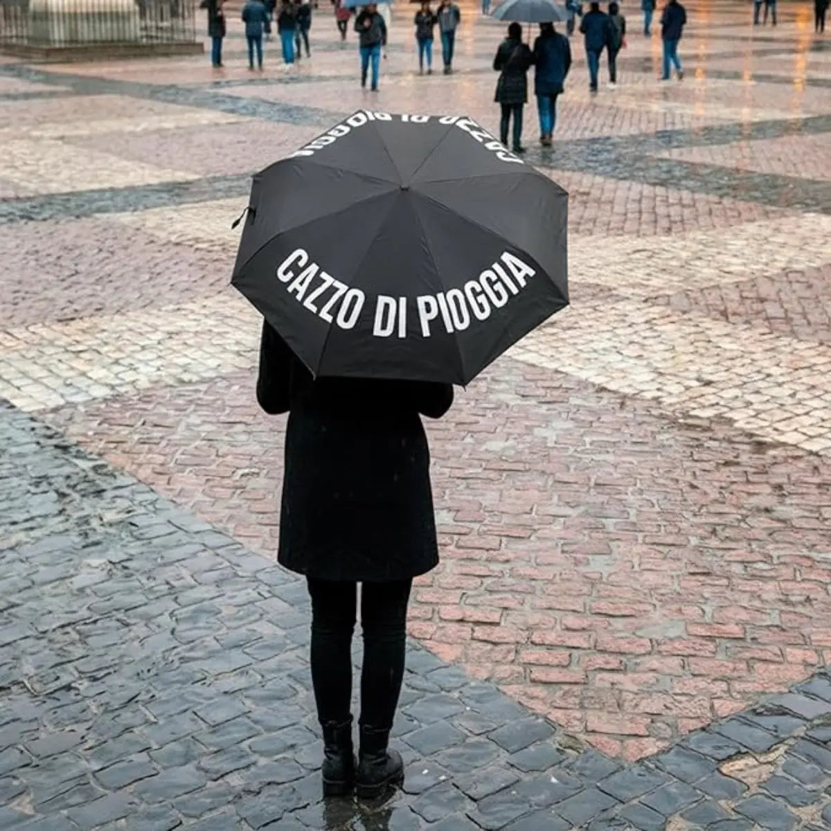 Donna vestita di nero che tiene in mano ombrello nero Cazzo di pioggia. Sfondo piazza di una città.
