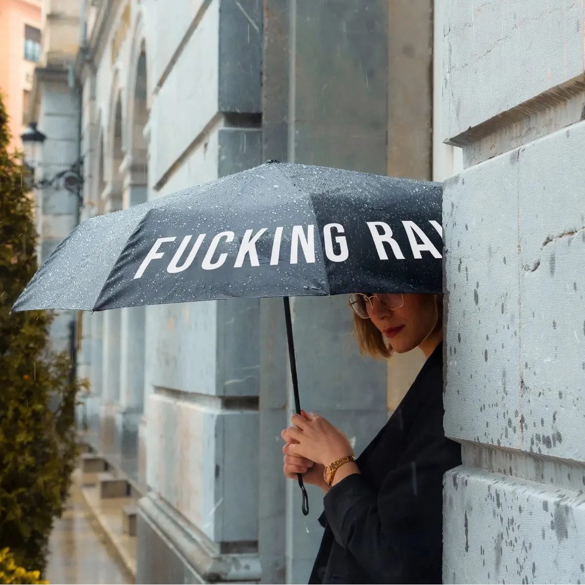 Donna vestita di nero che tiene in mano ombrello nero fucking rain. Sfondo monumento.