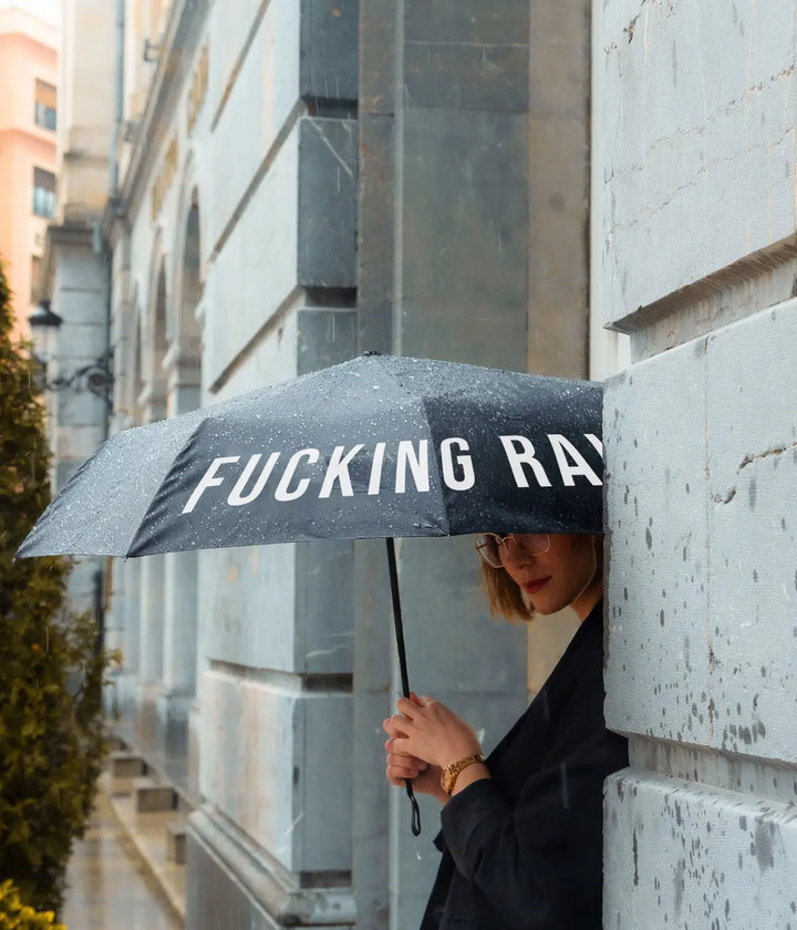 Donna vestita di nero che tiene in mano ombrello nero fucking rain. Sfondo monumento.