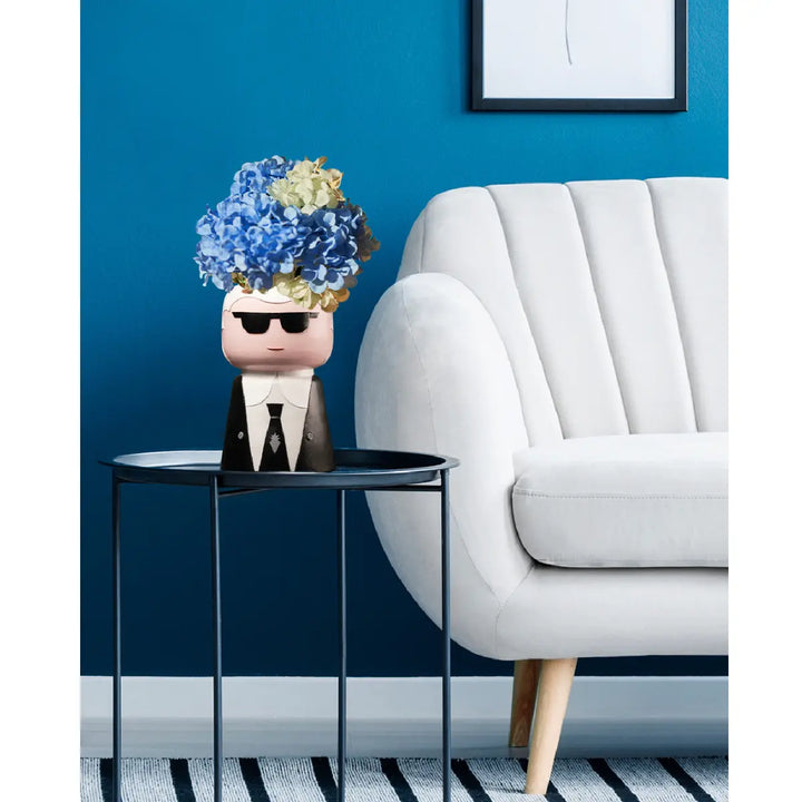Vaso Style che raffigura Karl Lagerfeld con dentro ortensie, appoggiato su tavolino blu. Sfondo blu
