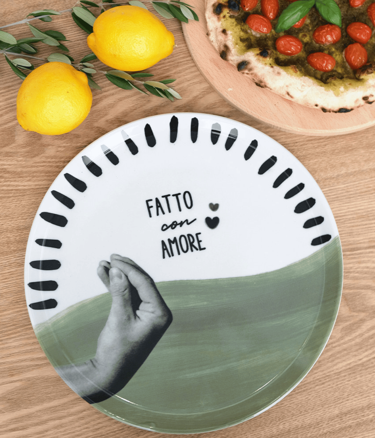 Piatto metà verde e metà bianco con decorazioni bordo e scritta neri. Sfondo legno, pizza e limoni.
