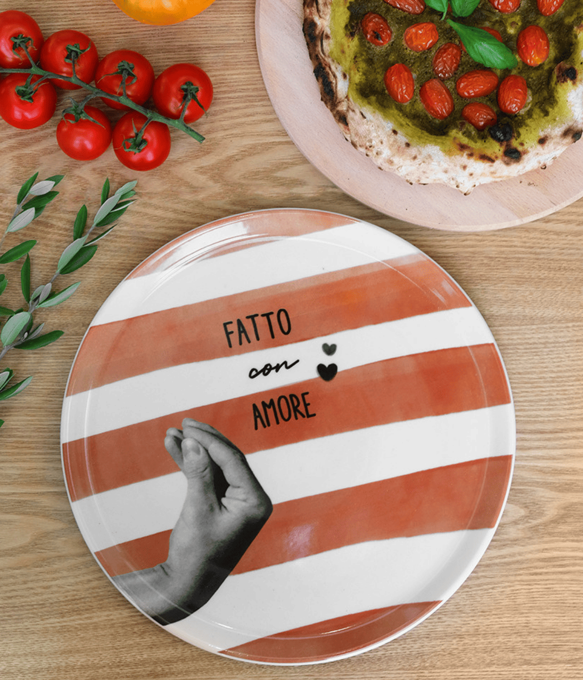 Piatto bianco con mano grigia, righe terracotta, scritta e cuori neri. Sfondo legno e alimenti.