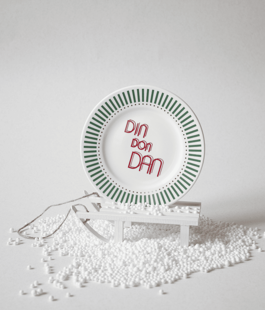 Piatto con scritta Din Don Dan e decorazioni verdi con puntini oro, appoggiato su slitta bianca e polistirolo. Sfondo bianco.
