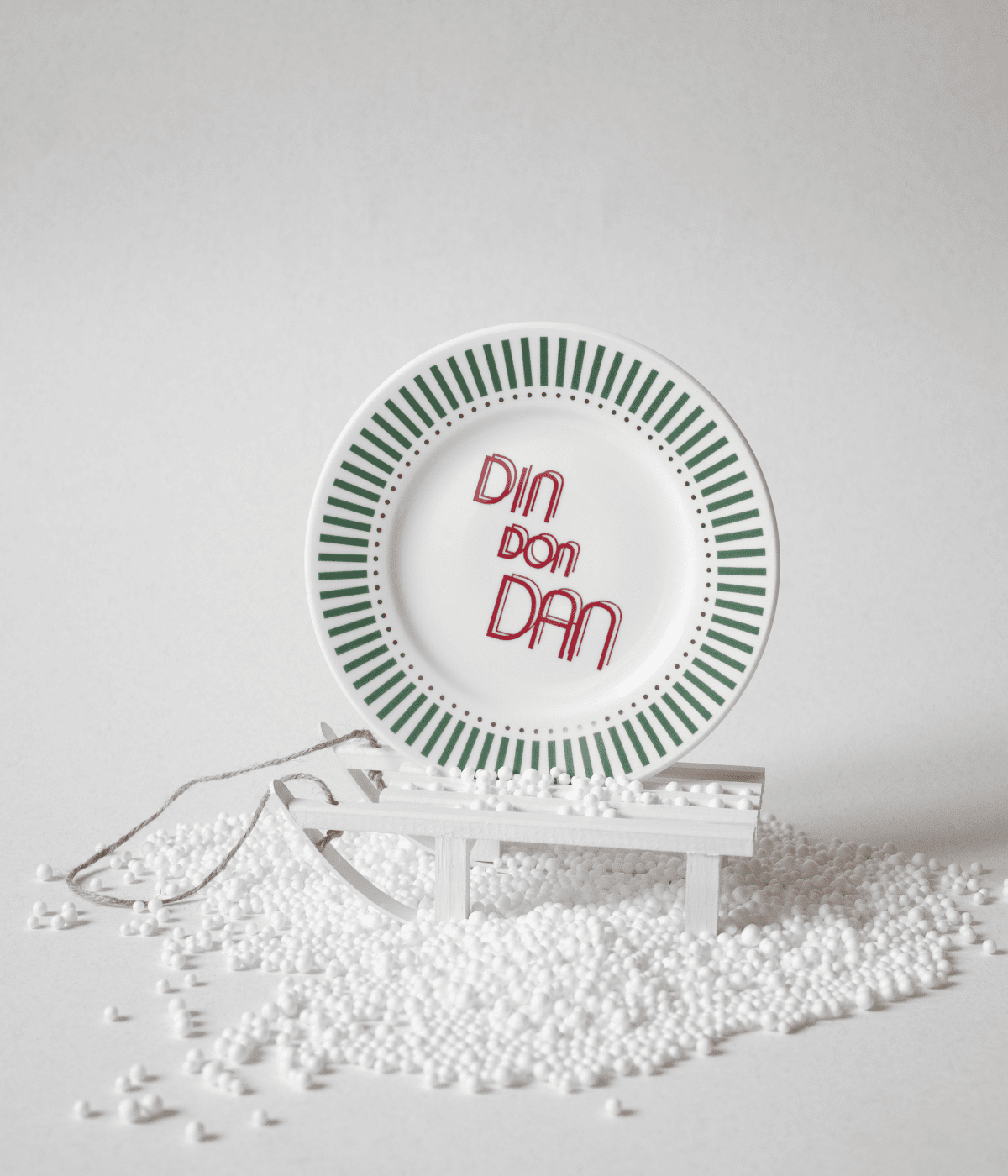 Piatto con scritta Din Don Dan e decorazioni verdi con puntini oro, appoggiato su slitta bianca e polistirolo. Sfondo bianco.