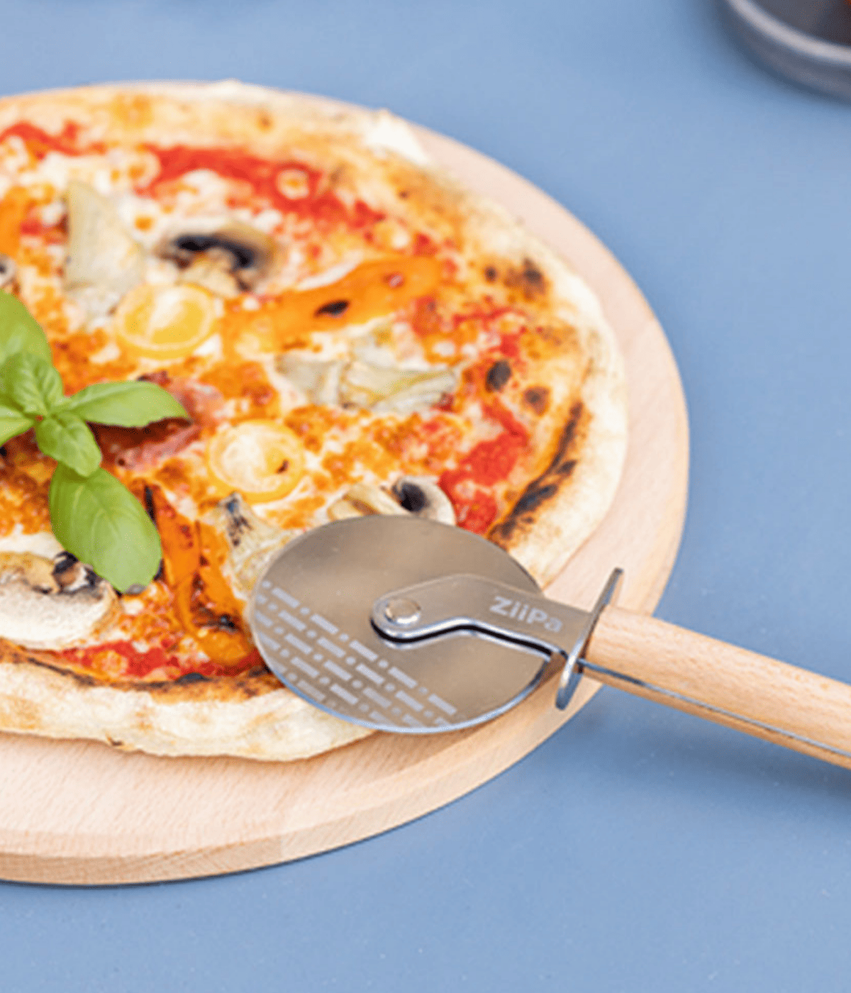 Pizza con appoggiata rotella grigia, con manico marrone e scritta Ziipa. Sfondo azzurro.