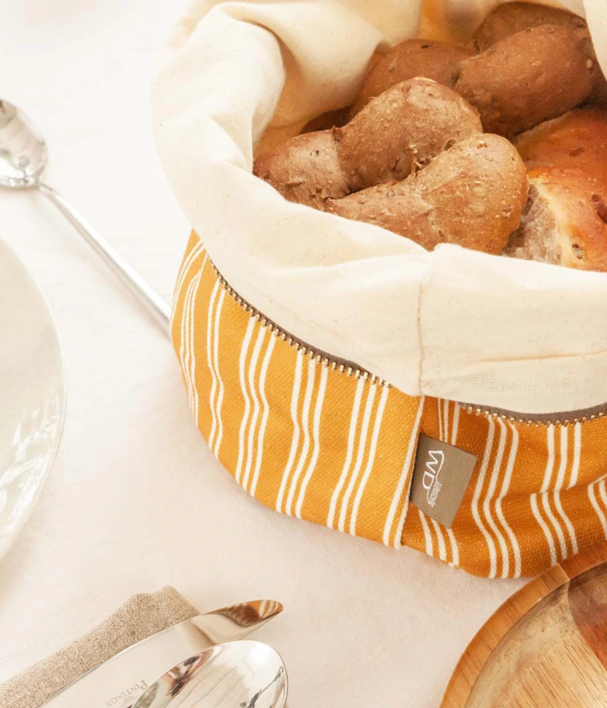 Un sacchetto portapane gessato ocra con cerniera e pane dentro. Sfondo tavola con tovaglia
