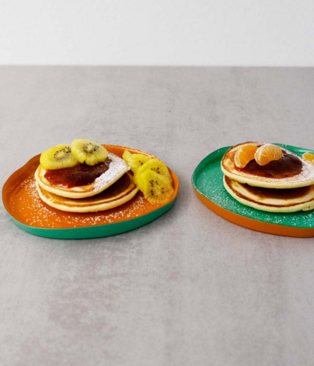 Due piatti colorati Verde e arancione con pancake e frutta fresca. Sfondo tavolo grigio