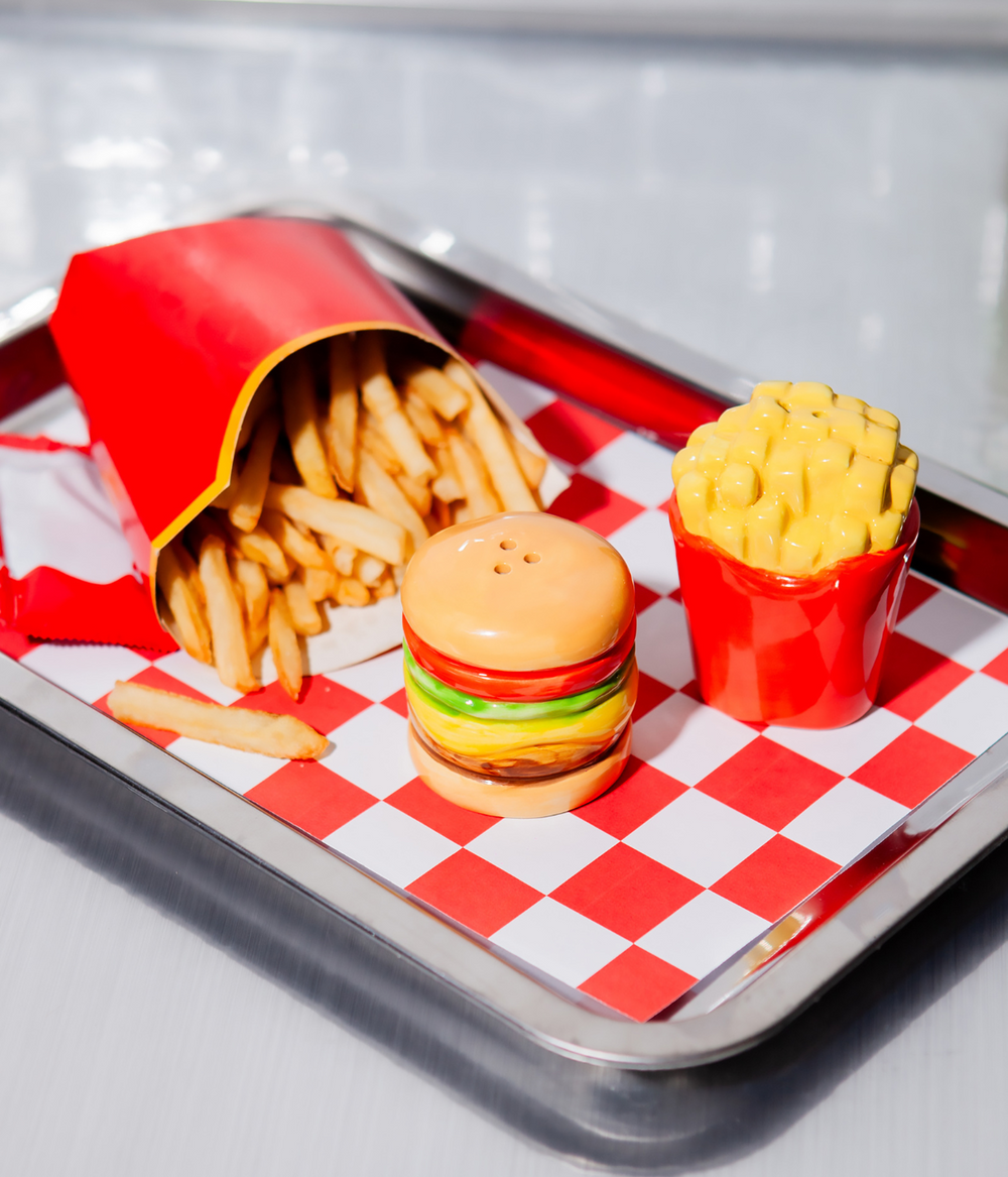 Un vassoio con tovaglietta. Sopra patatine fritte e due portaspezie a forma di hamburger e patatine