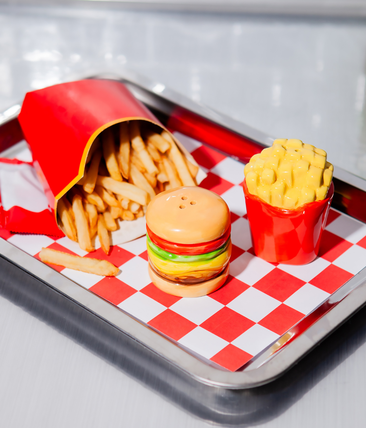 Un vassoio con tovaglietta. Sopra patatine fritte e due portaspezie a forma di hamburger e patatine