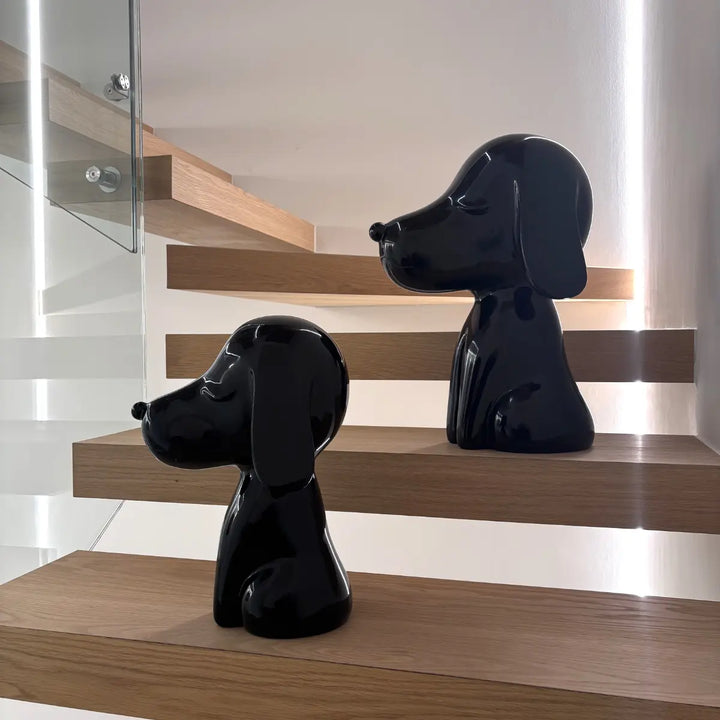 Due statue cani nere appoggiate su scale di legno e vetro. Sfondo muro bianco e luci