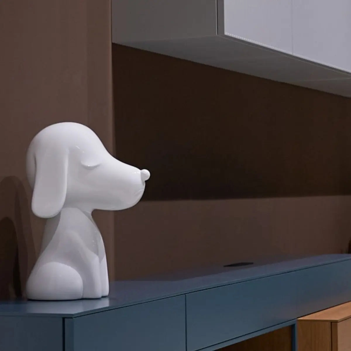 Statua Arturo bianca appoggiata di profilo su mobile consolle blu. Sfondo marrone e mobile bianco