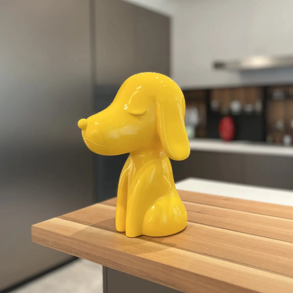 Statua Arturo Giallo appoggiata su piano cucina marrone. Sfondo mobili cucina bianco e grigio