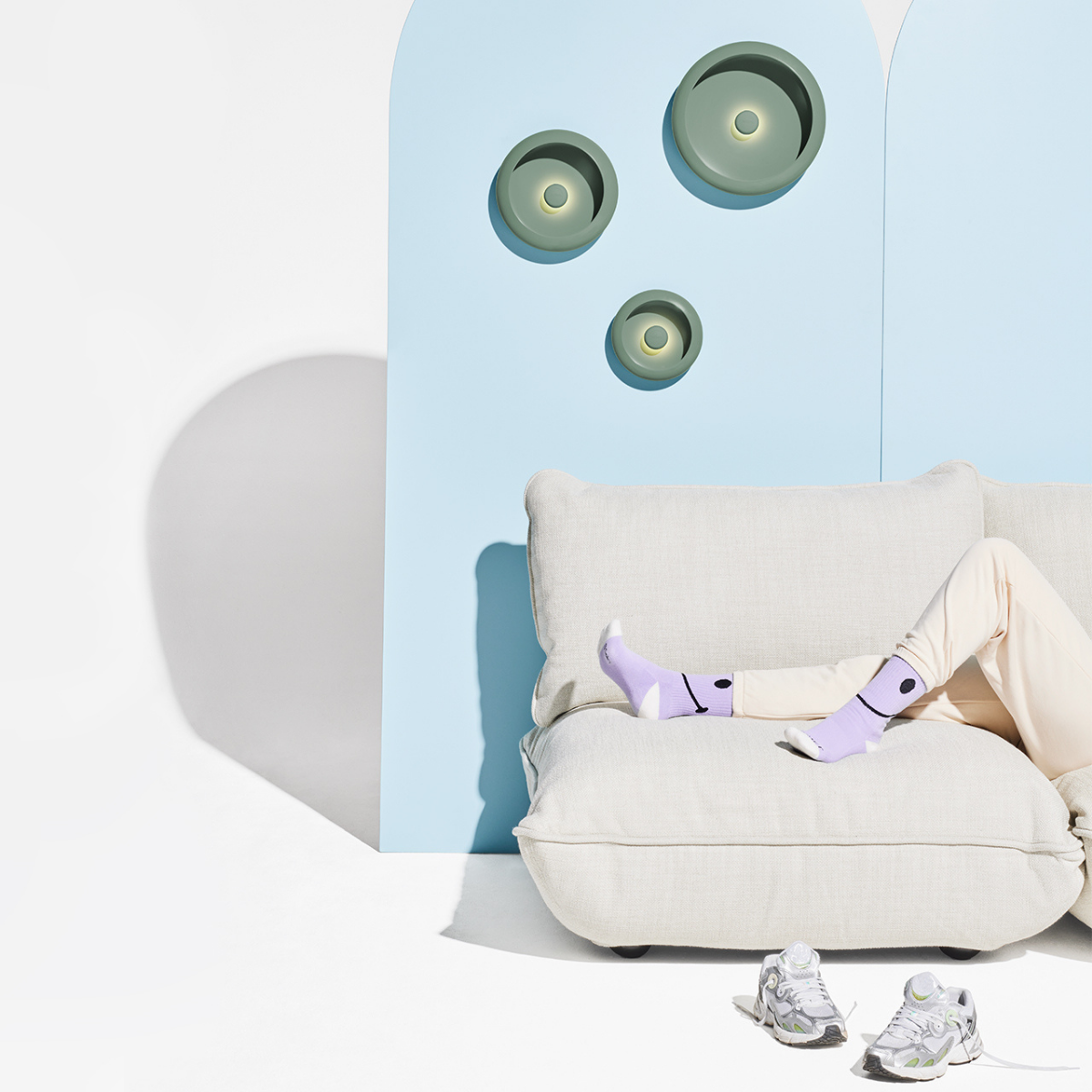 Tre lampade rotonde accese appese su muro azzurro. Sfondo divano, donna e scarpe. Sfondo bianco