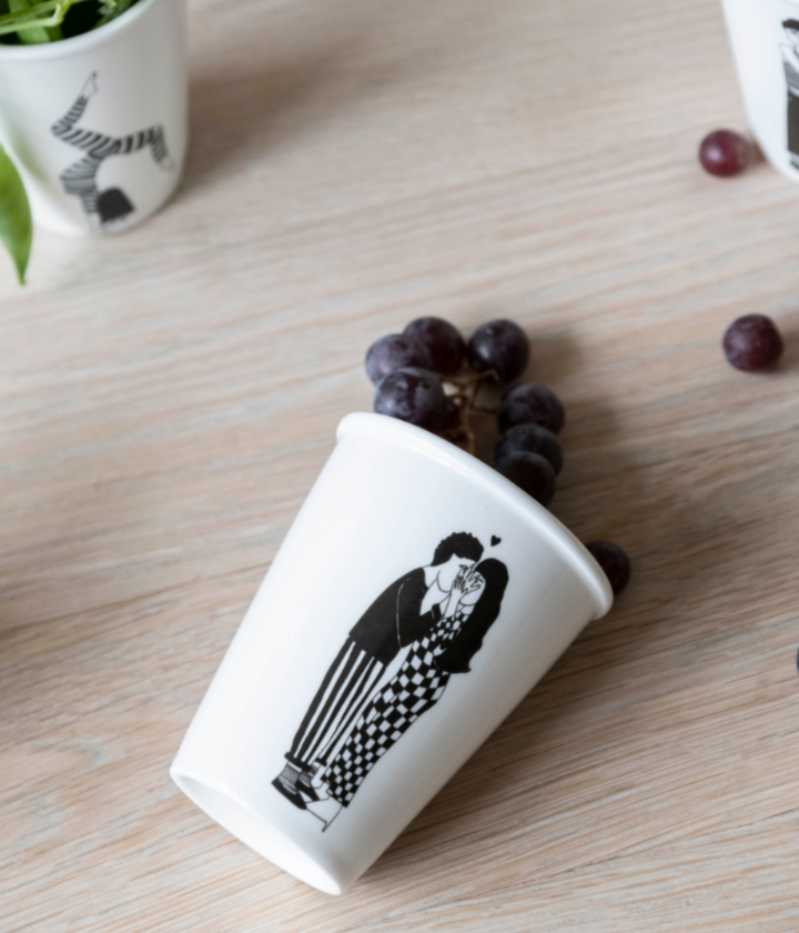 Tazza con coppia che si bacia di nascosto. Chicchi d'uva che escono dalla tazza. Sfondo tavolo.