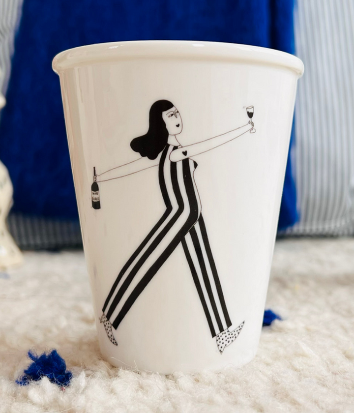 Tazza bianca con ragazza che tiene in mano la bottiglia e bicchiere mezzo pieno. Sfondo tappeto