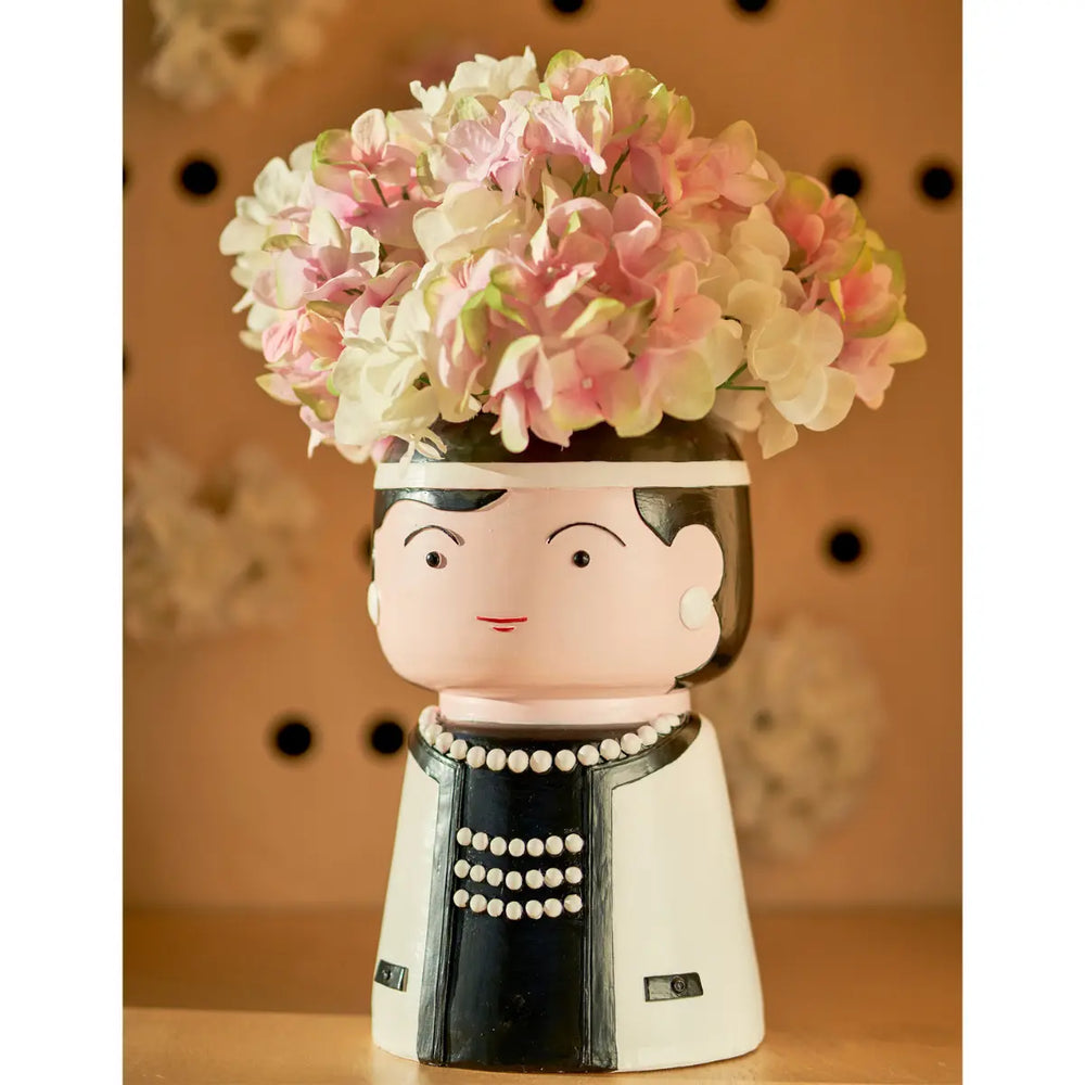 Vaso che raffigura Coco Chanel con dentro ortensie rosa e bianche. Sfondo marrone