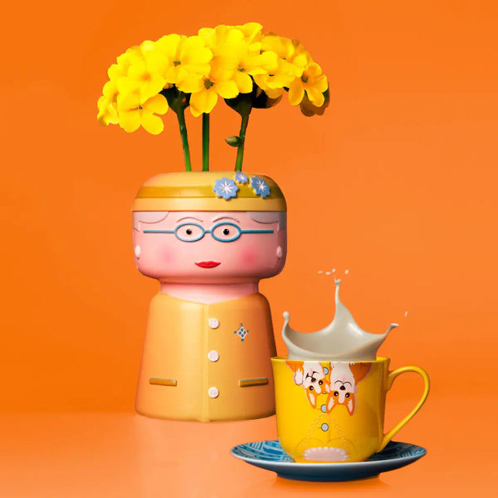 Vaso raffigurante la regina con fiori gialli e tazza con disegno Corgy. Sfondo arancione
