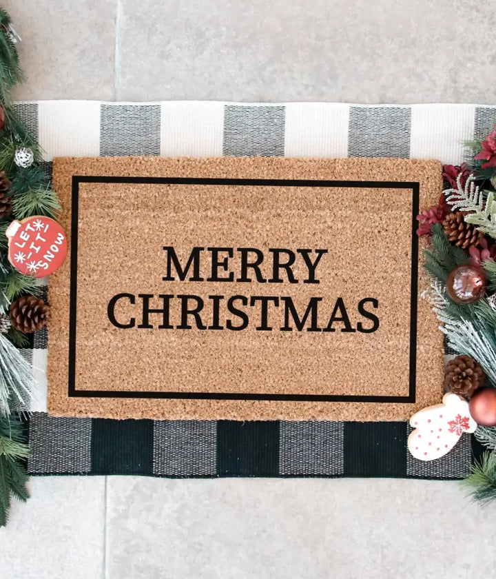 Zerbino Merry Christmas e cornice nera. Tovaglietta nera e bianca con rami di pino. Sfondo bianco.