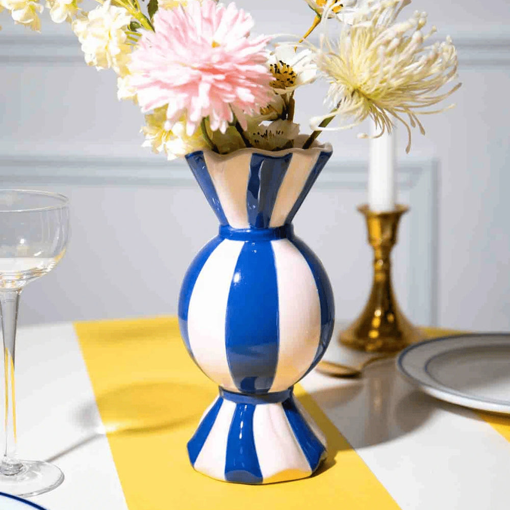 Vaso funfair a forma di caramella blu con fiori su tavolo giallo e bianco.