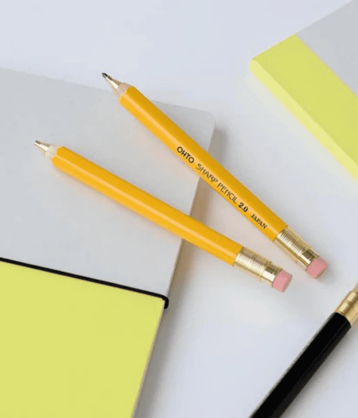 Due matite gialle appoggiate su quaderno bianco e giallo. Una con mina e una senza. Sfondo bianco.