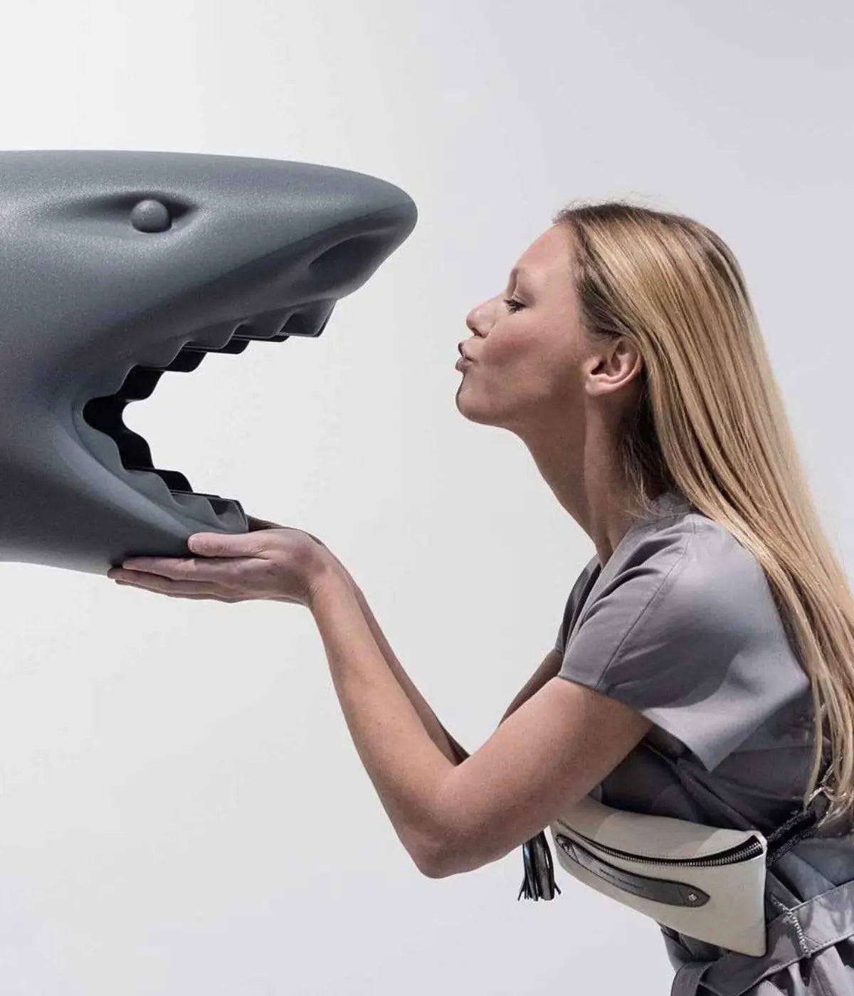 Donna che da un bacio allo squalo grigio con la bocca aperta. Sfondo grigio chiaro