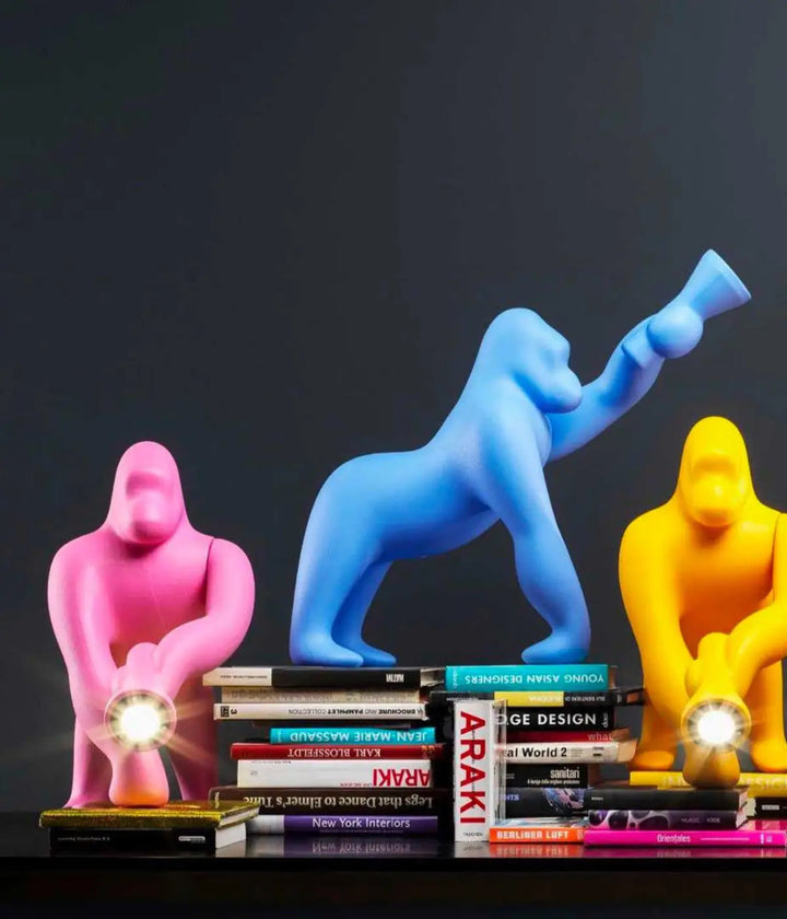 Tre lampade a forma di Kong, fuxia, rosa, giallo. Tutte appoggiate su libri e scrivania. Sfondo nero