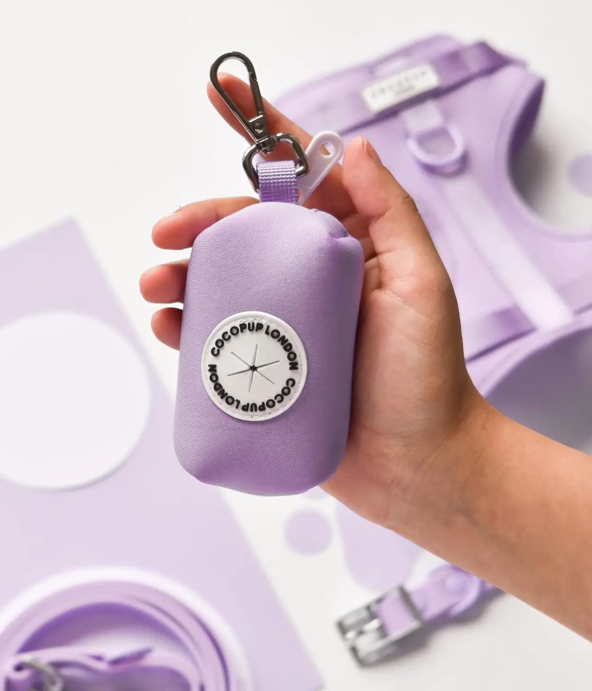 Porta Sacchetti lilla tenuto in mano, con collare e guinzaglio abbinati sullo sfondo.