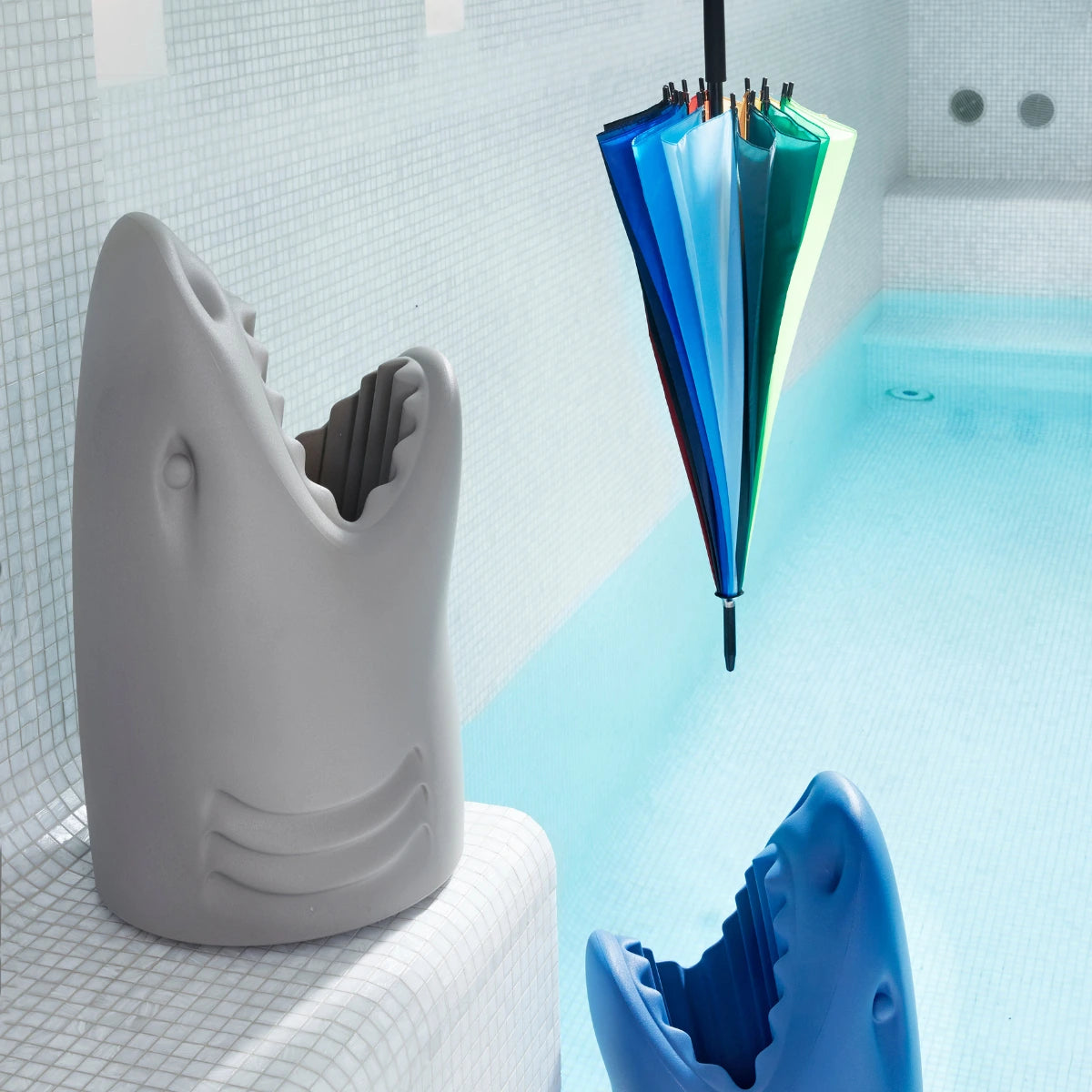 Due squali portaombrelli uno grigio, uno azzurro, in piscina. Cercano di catturare un ombrello.