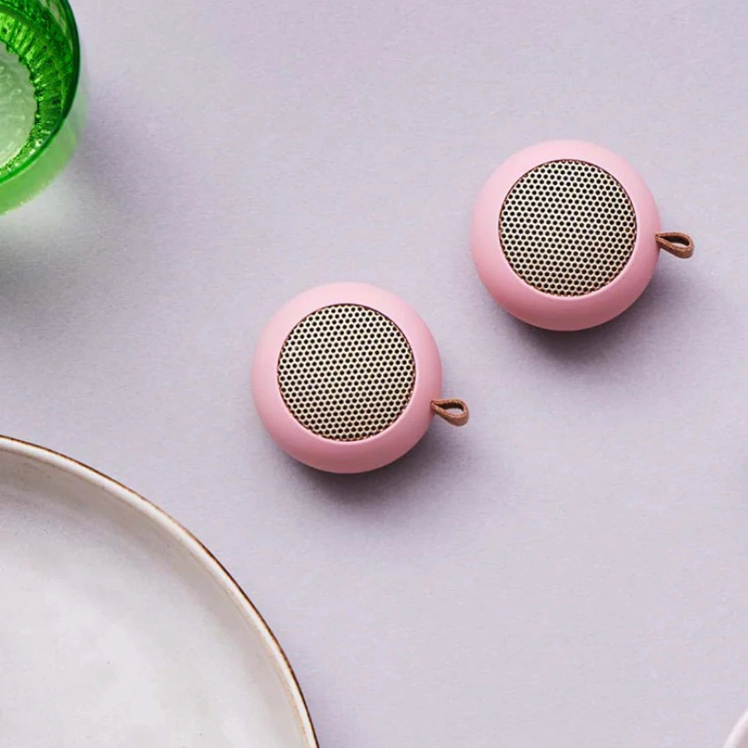 due mini casse audio portatili rosa su tavolo grigio.