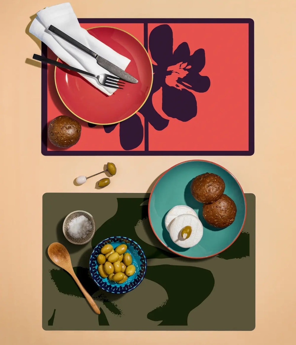 Due tovagliette con disegno floreale, una rossa e una verde con piatti sopra. Sfondo tavola beige