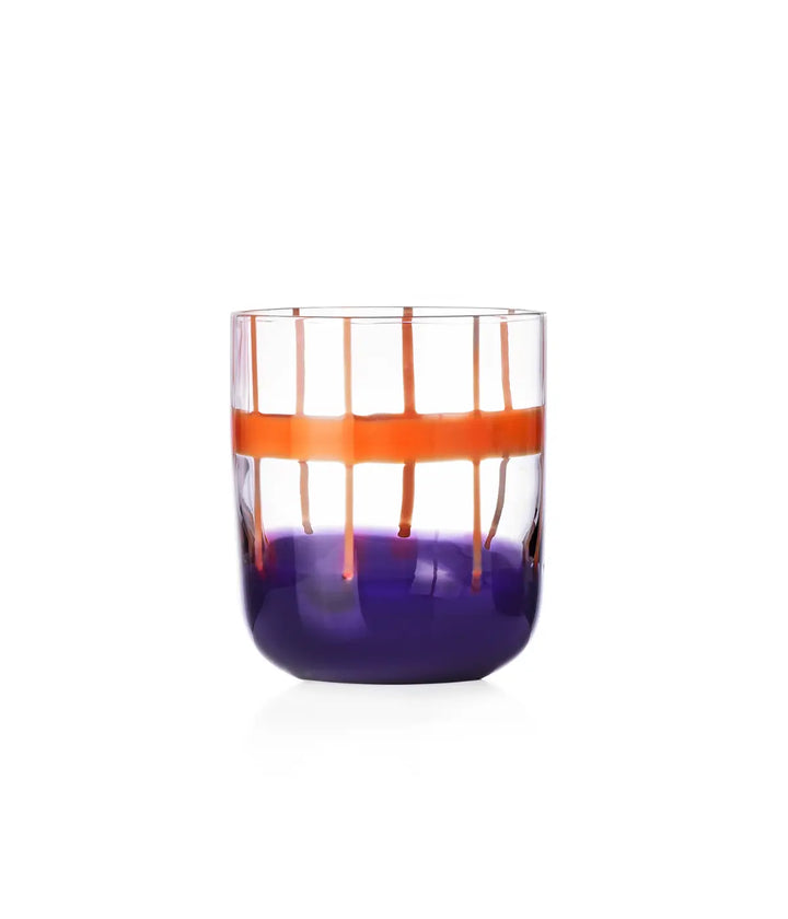 Un bicchiere in vetro trasparente con fondo viola e righe irregolari arancioni. Sfondo bianco